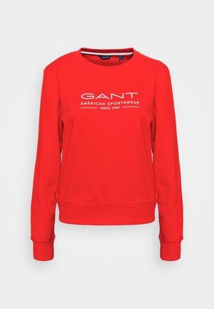Sudadera roja hecha de tela suave con cuello redondo, puños y dobladillo acanalados. Presenta un logo con texto blanco: "GANT AMERICAN SPORTSWEAR DESDE 1949."