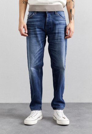 Tumma siniset farkut haalistuneella viimeistelyllä, kontrastitikkauksilla ja klassisella viiden taskun mallilla. Yhdistetty valkoisiin lenkkareihin.