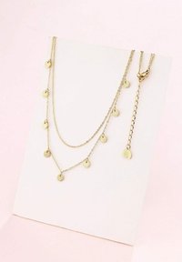 Collar de capas en tono dorado con charms circulares y un colgante en forma de hoja. Presenta delicados eslabones de cadena y cierre de langosta.