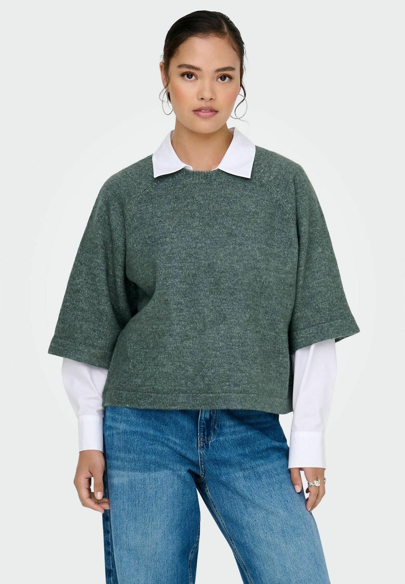 Groen gestructureerd oversized sweater met korte mouwen, gelaagd over een witte blouse met kraag, gecombineerd met blauwe jeans. Eenvoudig en casual ontwerp.