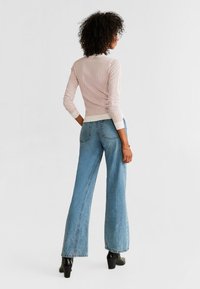 Jasnoróżowy sweter z dzianiny z ściągaczami, zestawiony z niebieskimi dżinsami o wysokim stanie i rozszerzanych nogawkach. Gładka struktura, dopasowany w talii. Czarna szpilki.