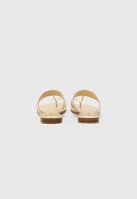 Ruskohartaisista nahka-sandaaleista, joissa on kaksi hoikkaa hihnaa, avonaiset takana ja litteä pohja, johon kuuluu pieni puu-aksentti. Sileä pinta ja minimaalinen yksityiskohtaisuus.