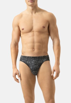 Torso maschile muscoloso che indossa slip neri con un sottile motivo paisley, in piedi contro uno sfondo grigio chiaro uniforme.