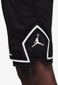 Black athletic shorts with a perforated texture, featuring a white Jumpman logo and contrasting white trim at the hem.