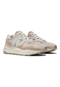 Beige Sneakers, die eine Kombination aus Wildleder und Mesh-Materialien aufweisen, mit einer strukturierten Sohle, Schnürdesign und einem übergroßen Logodetail an der Seite.