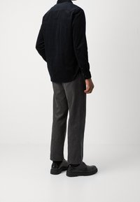 Camicia in velluto a coste nera con maniche lunghe, abbinata a pantaloni grigi a coste e scarpe nere stringate. Tessuto strutturato, vestibilità sartoriale.