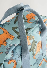 Blå dinosaur-tema ryggsäck med orange och gröna dinosaurtryck, vadderat material och slitstarka grå remmar.