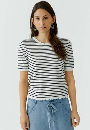 Vrouw met lang bruin haar, gekleed in een gestreept wit-zwart shirt met korte mouwen en een lichtblauwe spijkerrok met hoge taille en een strikceintuur.