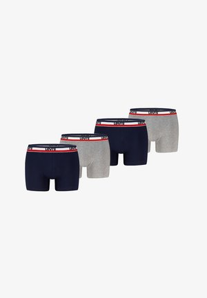 Muskolöser Mann trägt marineblaue Levi's Boxershorts mit weißem, rotem und marineblauem Bund, steht vor einem weißen Hintergrund.