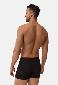 Schwarze Boxershorts mit rotem Bund, aus weichem Stoff gefertigt. Das Design bietet eine enge Passform und minimale Nähte für zusätzlichen Komfort.