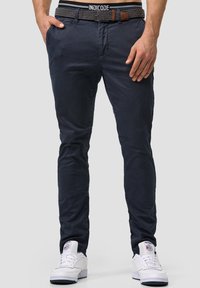 Navy slim-fit pants with a smooth texture, featuring side pockets and a black patterned belt with brown leather accents. Worn with white sneakers.