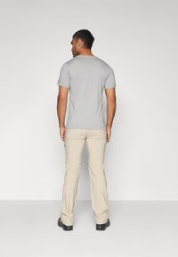 Camiseta gris de manga corta y pantalones beige llevados por una persona, vista desde la parte posterior. La camiseta es ajustada; los pantalones son ligeros y tienen bolsillos.