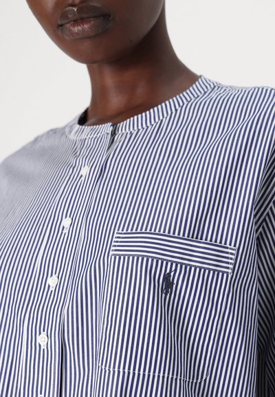 Camisa de botão riscada em algodão azul marinho e branco. Apresenta um decote redondo, um bolso frontal com um design riscado e bordado de logotipo distinto.