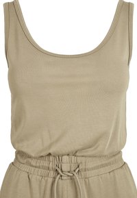 Débardeur beige en tissu doux et extensible. Il présente un col rond et une taille élastiquée avec cordon de serrage pour un ajustement ajustable.