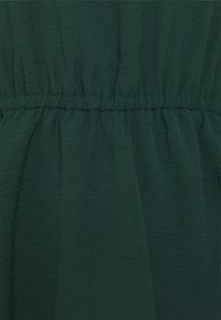 Tessuto verde testurizzato con vita elastica arricciata, caratterizzato da drappeggi morbidi e fluide e motivi subtili. Ideale per abbigliamento leggero.