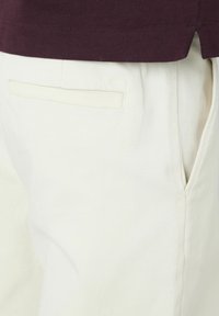 Pantalon en coton blanc avec une texture lisse, doté d'une poche arrière. Associé à une chemise violet foncé au niveau de la taille.
