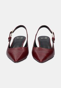 Zapatos slingback de cuero burdeos con punta afilada y detalle de hebilla dorada en la correa del tobillo; textura suave, diseño minimalista.