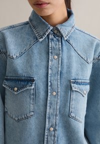 Lichtblauw denim overhemd met een kraag, twee borstzakken en zilverkleurige drukknopen. Kenmerkt zich door een textuurstof en contrasterende stiksels.