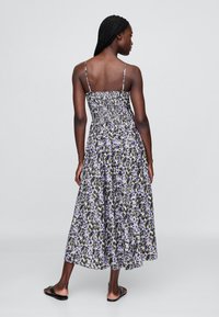 Florales Midikleid mit breiten Schulterträgern, gerafftem Oberteil und fließendem Rock in lila, grün und weißen Mustern. Rückansicht gezeigt.