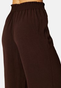 Bruine wijde broek van textuurstof met een elastische ruchesband, beschikt over een losse pasvorm voor comfort en bewegingsgemak.