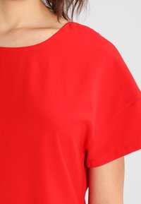 Červený tričko s krátkým rukávem a širokým, zaobleným výstřihem. Hladká tkanina s měkkou strukturou, navrženo pro volný střih.