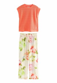 Coral, short-sleeved top with a textured pattern above white floral pajama pants featuring pastel roses and green leaves, elastic waist with drawstring.