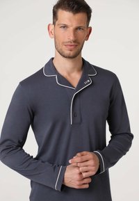 Polo a maniche lunghe di colore blu navy con piping bianco sul colletto e sui polsini, dotato di una finitura con tre bottoni e un accento del logo.