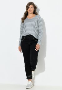 Camisa de rayas gris y blanca de manga larga combinada con jeans negros con tachuelas decorativas en los puños y zapatillas blancas.