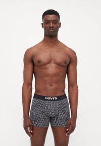 Crne bokserice s geometrijskim bijelim uzorkom, s crnim pojasom na kojem je logo "Levi's". Glatka tekstura, uski kroj.
