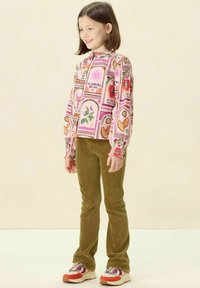 Chemise à manches longues avec un design rose à motifs floraux et en forme de cœur, associée à un pantalon en velours côtelé vert olive et des baskets colorées.