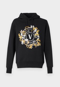 Juodas gobtuvas su apvalia, puošnia grafika baltos ir auksinės spalvų kombinacijoje, kurioje yra užrašas "Versace Jeans Couture" ir centrinė raidė "V".
