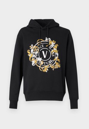 Czarna bluza z kapturem z okrągłym, ozdobnym nadrukiem w białym i złotym kolorze, zawierającym napis "Versace Jeans Couture" oraz centralną literą "V".