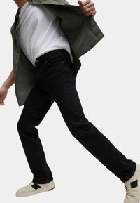 Jeans de mezclilla negra de corte slim, combinados con una camiseta blanca y una camisa verde. Los zapatos son blancos con un acento verde.