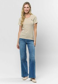 Svītrainā ribota T-kreklu bežā un baltā krāsā ar apaļu kakla izgriezumu. Savairots ar izsistiem ziliem džinsiem un gaišas krāsas austām kurpēm.