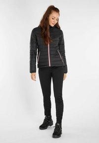 Zwarte pufferjack met roze ritsaccenten, voorzien van een hoge kraag en zijzakken, gecombineerd met zwarte broek en wandelschoenen.