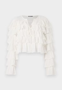 Hvit cropped bluse med flere horisontale volanger langs ermene og kroppen, laget av et lett og gjennomsiktig stoff. Knytedetalj foran.