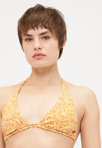 Geel halterbikini top met abstracte witte en roze patronen. Heeft een V-vorm en geplooide details onder de buste.