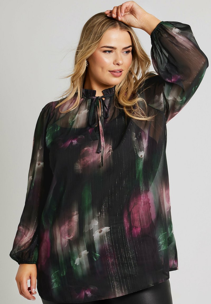 Maglia leggera nera con stampa floreale in viola, verde e bianco. Presenta maniche a sbuffo e un dettaglio con fiocco al collo. Tessuto testurizzato con lucentezza.