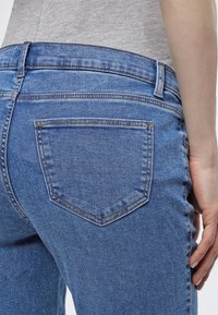 Κοντινό πλάνο ενός ατόμου που φορά μεσαίου μπλε τζιν τζιν με πίσω τσέπη και γκρι τοπ που είναι μαζεμένο μέσα.