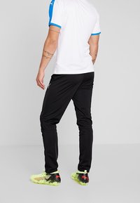 Puma sportsoutfit bestående af en hvid skjorte med blå accenter, sorte bukser og lyse gule sko med netdetaljer.