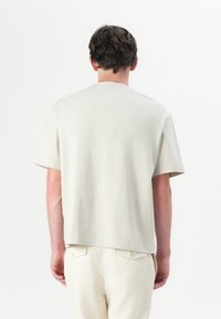 Helles Beige, kurzärmeliges T-Shirt aus weichem Baumwollmaterial; verfügt über einen Rundhalsausschnitt, einen leicht lockeren Schnitt und ein schlichtes Rückendesign.