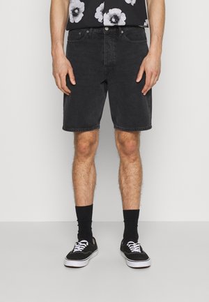 Svarta denimshorts med rak skärning, med fem fickor och bälteshällor. Bärs med svarta strumpor och kanvassneakers.
