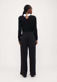 Pull noir à manches longues, avec un col blanc et une ouverture en forme de clé au dos. Associé à un pantalon noir ample.