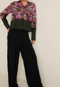 Cropped, collared blouse with a floral pink and green pattern, paired with black, wide-leg trousers featuring side pockets and a smooth texture.