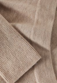 Tissu beige tricoté présentant une texture lisse et un motif côtelé, avec des nuances variées et une apparence chaleureuse. Convient pour vêtements ou accessoires.