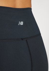 Leggings neri realizzati in materiale elastico, con una texture liscia, un design aderente e un piccolo logo riflettente New Balance all'orlo della vita.