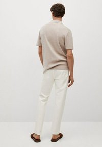 Polo beige à manches courtes avec un col plat, texture légère, associé à un pantalon blanc et des sandales brunes.