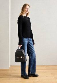 Pull noir à côtes avec des manches longues, associé à un jean bleu à jambes larges. Accessoirisé avec un sac à dos en cuir noir avec une poche zippée.