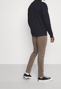Granatowy sweter, khaki spodnie, czarne trampki. Materiał wydaje się być z mieszanki bawełny, buty mają białe sznurowadła i gumowe podeszwy.