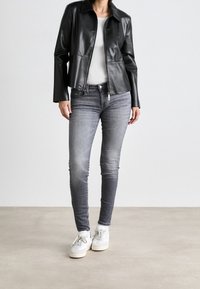 Chaqueta de cuero negra con cuello de presión, jeans ajustados grises y zapatillas blancas. Textura suave, con cierre de cremallera y detalles sutiles.